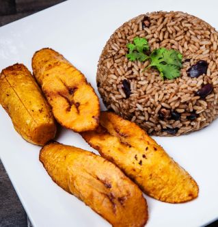 A savory plate of rice and beans with fried plantains on a white plate, garnished with parsley.